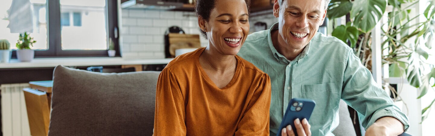 Zwei Personen sitzen gemeinsam auf einem Sofa und blicken zusammen auf ein Handy.