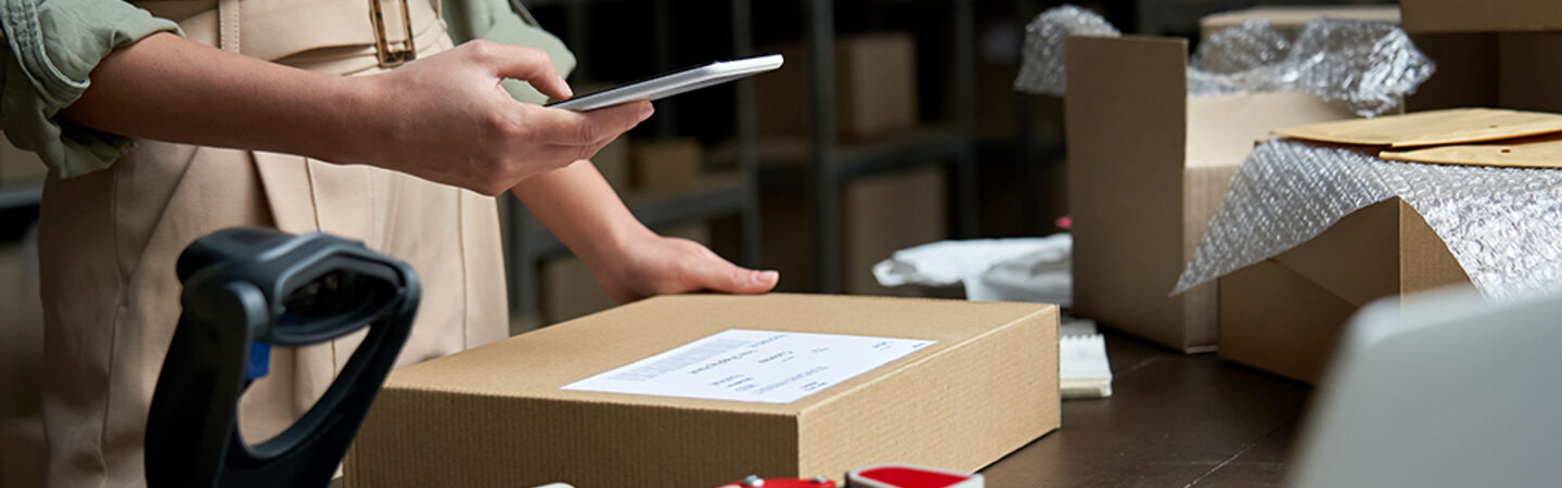 Frau im Paketlager breitet ein Paket für den Versand vor.