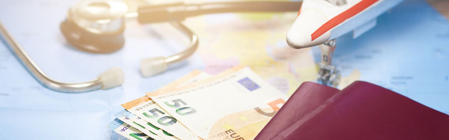 Artikelbild Weltkarte mit Geldscheinen, Reisepass, kleinem Flugzeug und Stethoskop