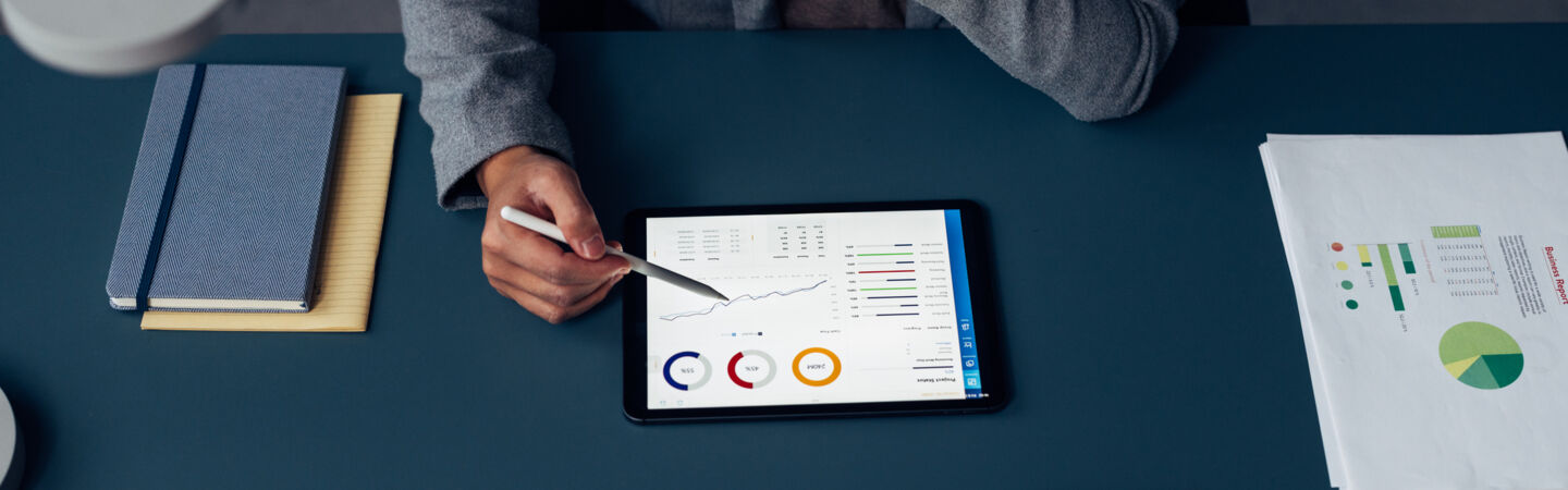 Artikelbild Person sitzt vor Tablet am Schreibtisch und analysiert die Zahlen auf dem Tablet