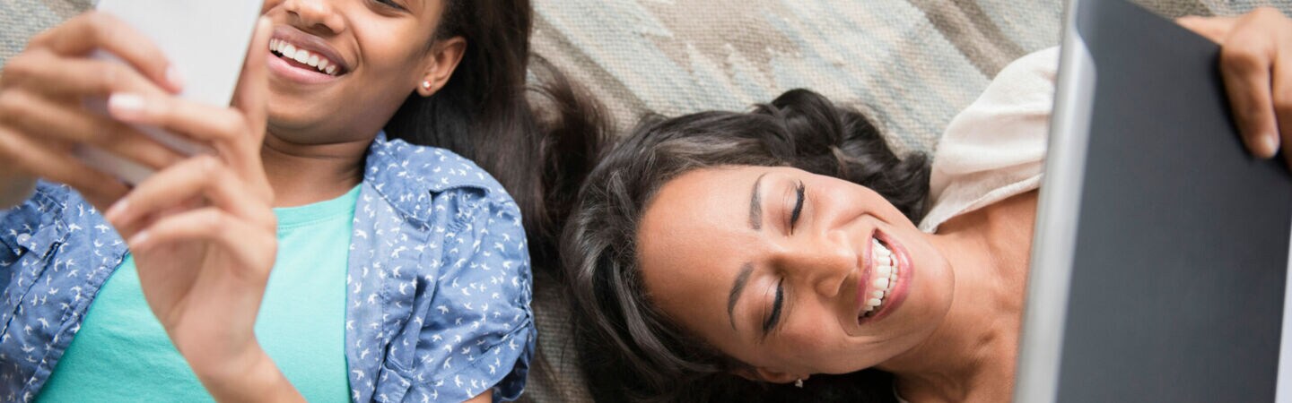 Mother and daughter laying on carpet using cell phone and digital tablet