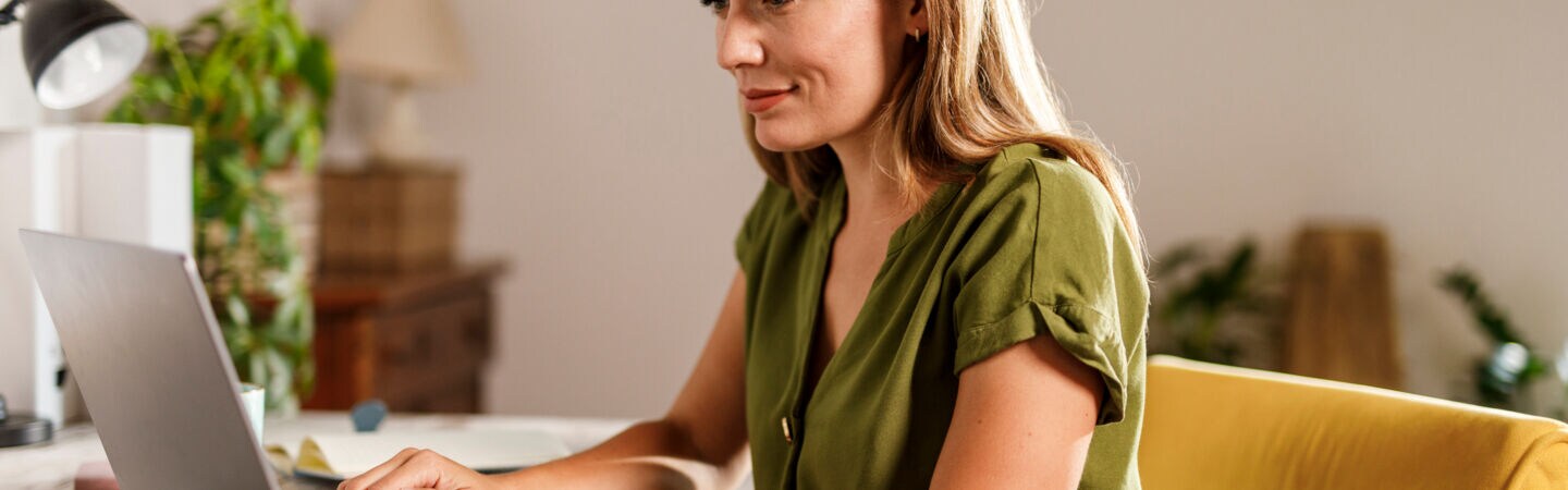 Eine Frau sitzt an einem Tisch vor einem Laptop und legt ihre Hände auf die Tastatur.