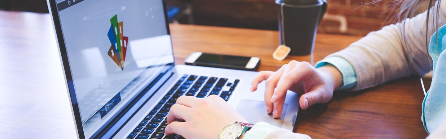 Person arbeitet an einem Laptop in einem modernen Büro mit Notizblock, Smartphone und Teetasse auf dem Schreibtisch