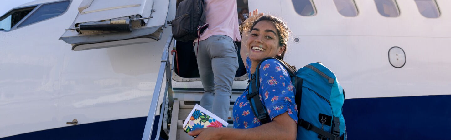 Person steht vor dem Flugzeug und hat einen Backpacker auf dem Rücken und seinen Reisepass in der Hand