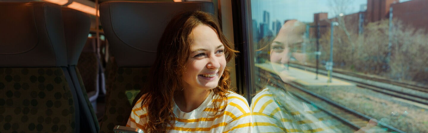 Person sitzt in der Bahn am Handy und schaut aus dem Zugfenster