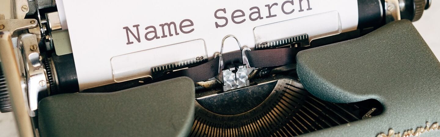 Nahaufnahme einer klassischen Schreibmaschine mit einem Blatt Papier, auf dem der Text ‚Name Search‘ steht. Das Bild symbolisiert die Suche nach einem Namen, etwa für ein Unternehmen, Produkt oder Projekt