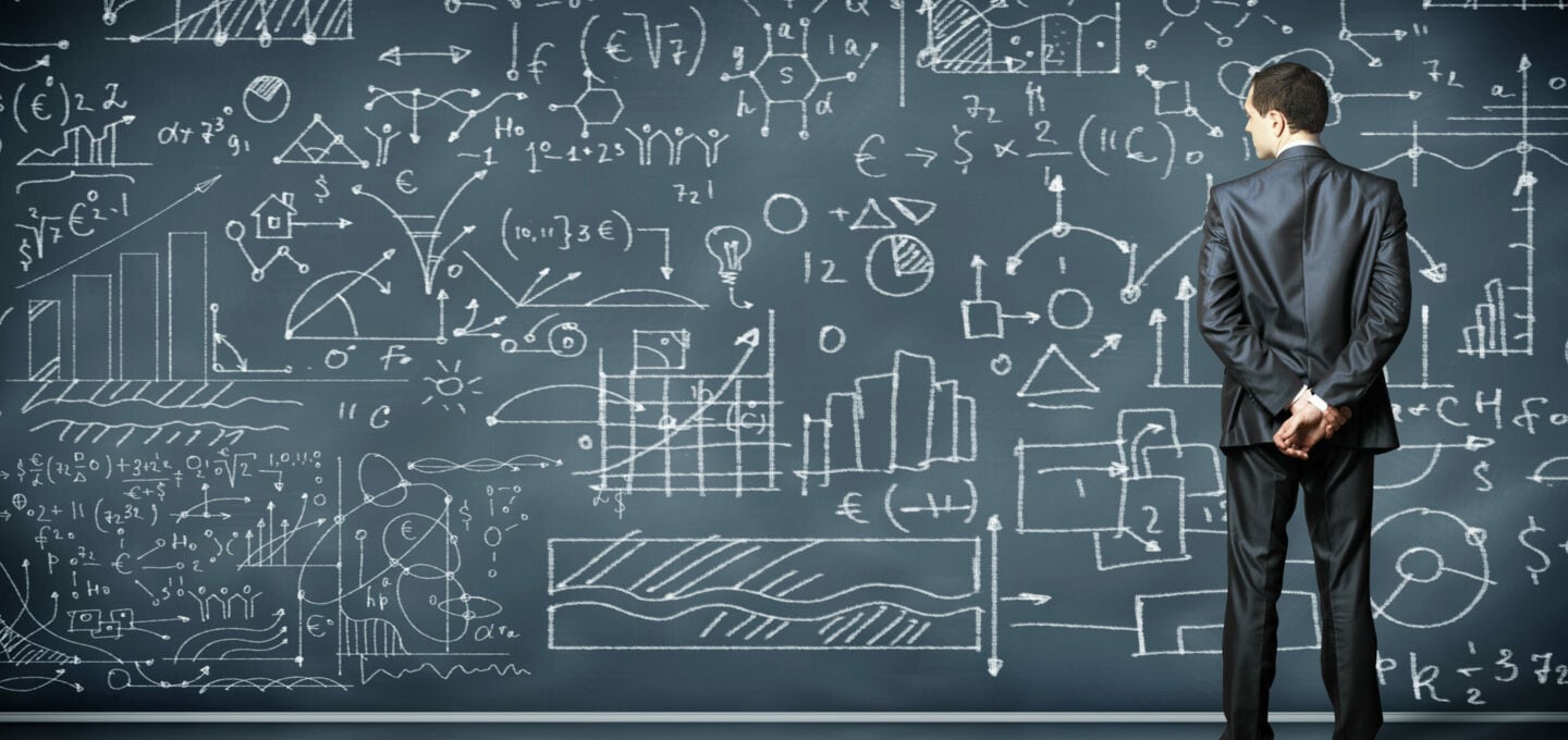 Eine Person steht vor einer Tafel mit mathematischen Formeln und Diagrammen