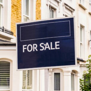 Schild mit der Aufschrift „For Sale“ vor einer Häuserfassade in der Stadt