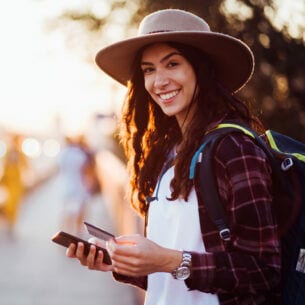 Eine lachende junge Frau mit Smartphone und Kreditkarte in der Hand