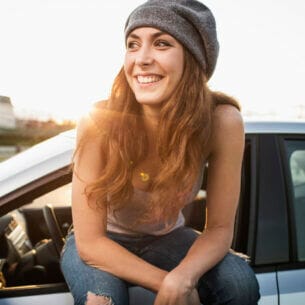 Eine junge Frau sitzt lächelnd vor einem Auto