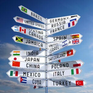 Wegweiser mit Nationalflaggen verschiedener Länder vor blauem Wolkenhimmel