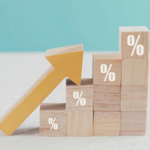 An treppenförmig aufgebauten Bauklötzen mit aufgedruckten Zinszeichen lehnt ein nach oben zeigender Pfeil