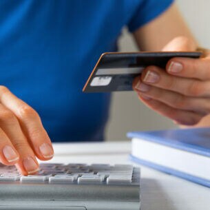 Eine Person hält eine Kreditkarte in der Hand und tippt mit der anderen Hand Daten auf einer Tastatur ein