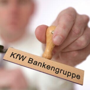 Mann hält Stempel mit der Aufschrift KfW Bankengruppe in der Hand.