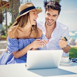 Ein fröhliches Pärchen sitzt im Urlaub am Laptop