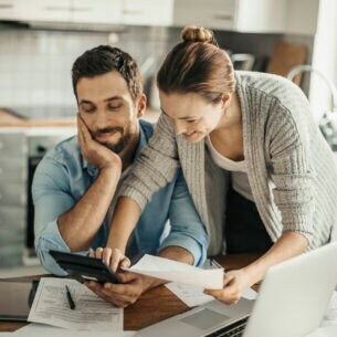 Ein junges Paar am Küchentisch mit Laptop, Taschenrechner und Papieren