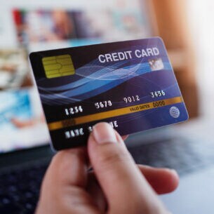 Zwei Hände, eine Kreditkarte und ein Flugzeugmodell haltend, vor einem Laptopbildschirm