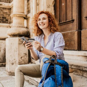 Junge Frau auf einer Treppe sitzend mit Kreditkarte und Smartphone in der Hand