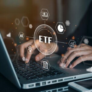 An einem Laptop tippende Hände, davor eingeblendet verschiedene Symbole zu ETFs