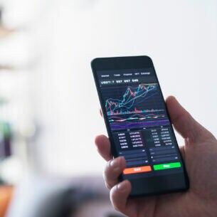 Ein Smartphone in der Hand einer Person mit Aktienkursübersicht auf dem Display