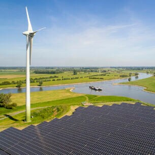 Blick auf eine grüne Landschaft und einen Fluss hinter einem Windrad und einer großen Solaranlage