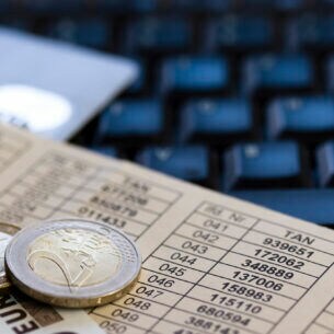 Euromünzen und ein Euroschein liegen auf einem Zettel, auf dem Zahlen in Tabellenform stehen