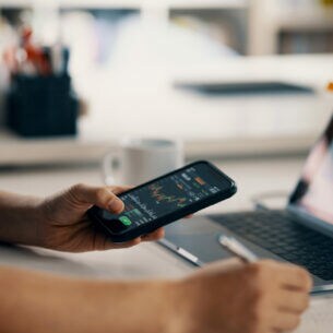 Eine Person hält ein Smartphone in der Hand, auf dem ein Börsenkurs abgebildet ist.