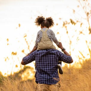 Rückansicht einer erwachsenen Person, die ein Kind auf den Schultern trägt