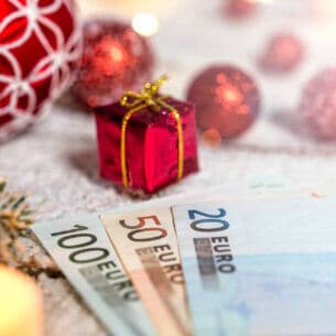 Drei verschiedene Euro-Geldscheine liegen aufgefächert zwischen drei Geschenkpaketen mit rotem Geschenkpapier und weißer Schleife