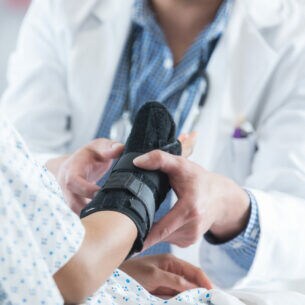 Eine Ärztin legt einer jungen Frau am rechten Arm eine schwarze Armmanschette um.