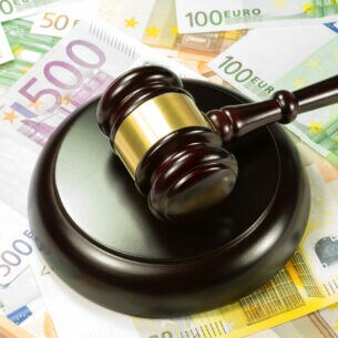 Unterschiedliche Euroscheine liegen verteilt auf einem Tisch, darauf befindet sich ein Richterhammer