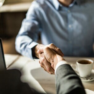 Zwei Personen sitzen sich am Tisch gegenüber und schütten Hände