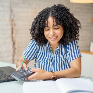 Eine Frau sitzt am Schreibtisch und hält einen Taschenrechner in den Händen