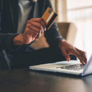 Eine Person sitzt am Laptop und hält eine Bankkarte in der Hand