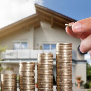 Nach rechts höher werdende Münzstapel. Im Hintergrund ein Einfamilienhaus.