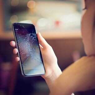Eine Person betrachtet das Display ihres Smartphones, das zersprungen ist.