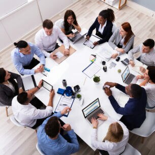 Eine Gruppe von zwölf Personen sitzt mit Laptops an einem Tisch.