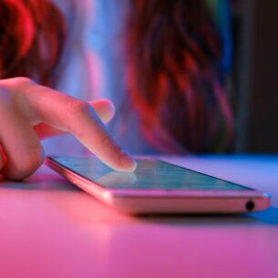 Eine Person tippt mir ihrem Finger auf das Display eines Smartphones, das auf einem Tisch liegt.