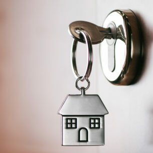 Ein Schlüssel mit Anhänger in Form eines Hauses steckt in einem Türschloss.