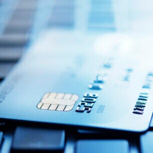 Blau getöntes Foto einer Kreditkarte, die auf der Tastatur eines Laptops liegt und deren Kreditkartennummer erkennbar ist.