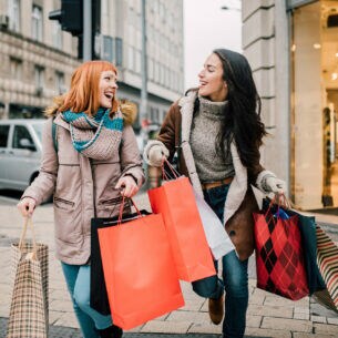 Zwei Personen gehen lachend mit Einkaufstüten über eine Straße.