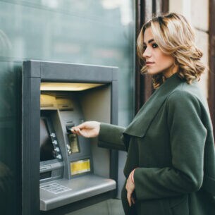 Eine junge Frau schiebt eine Karte in einen Geldautomaten