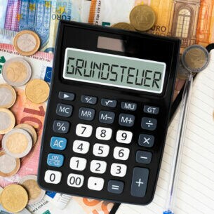 Ein Taschenrechner liegt auf Euroscheinen und Euromünzen, auf dem Display steht das Wort Grundsteuer.