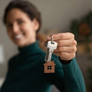 Eine Person hält lächelnd einen Schlüsselbund mit einem Anhänger in Form eines Hauses hoch.