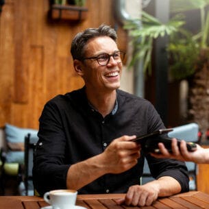 Ein Mann bezahlt mit seinem Smartphone kontaktlos in einem Café.