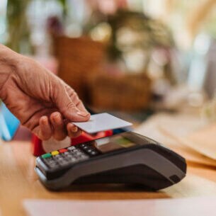 Eine Person hält eine Karte zum Bezahlen an ein Kartenlesegerät.