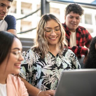 Mehrere junge Personen sitzen in einem Hörsaal um ein Laptop herum.