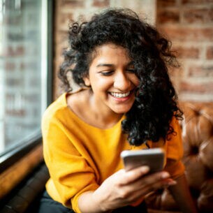 Eine Person sitzt auf einem Ledersofa und blickt lächelnd auf ihr Smartphone.