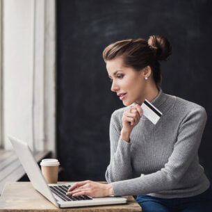 Eine Frau sitzt vor einem Laptop und hält eine Bankkarte in der Hand.