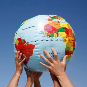 Mehrere Hände halten einen Ball mit Weltkugelmotiv in die Höhe.